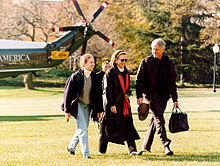 Man, same woman, and teenage girl walk across lawn after leaving a helicopter