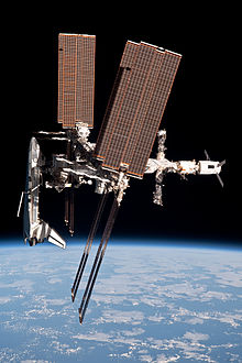 A side-on view of the ISS showing a Space Shuttle docked to the forward end, an ATV to the aft end and  Soyuz & Progress spacecraft projecting from the Russian segment.