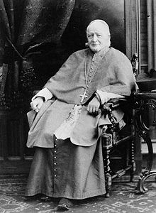 A seated elderly man in Roman Catholic priest's vestments.