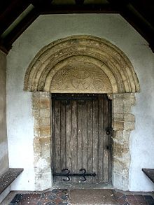 A plain wooden door over which is a round arch with a carved tympanum