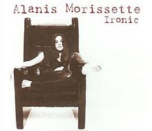 A barefoot white-skined woman is sitting on a big chair with armrests. She rests her right foot on the left armrest, while she crosses her left leg in front of her body. The background is white, and the words "Alanis", "Morissette" and "Ironic" are written in red letters at the upper right corner.