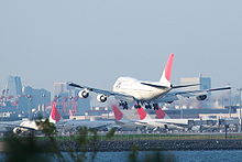 rear view of aircraft landing, with airport terminal and parked aircraft in the background