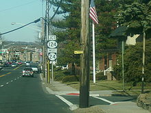 A two lane undivided road in a wooded residential area with roadside signs reading south Route 54, Atlantic City Expressway straight, and a four lane undivided road in a developed area with a sign on the right side of the road reading junction Route 124 west Route 24