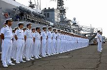Japanese sailors lined up on a quay in front of a warship.