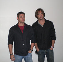 Two men wearing jeans and black shirts.
