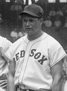A man is pictured from his belt up looking to the left of the camera. His button-down baseball jersey says "RED SOX" across it and he is wearing a baseball hat with a "B".