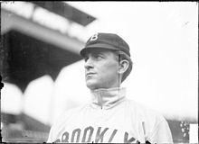 A man wearing a baseball cap and jersey with "Brooklyn" written across the chest looks to the left.