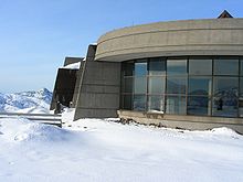 Surrounding a curved building with glass windows is a landscape of snow.