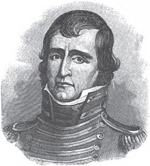 A man with dark hair wearing a high-collared, black military jacket
