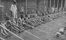 A row of more than a dozen children holding wooden looms stretches into the distance.