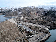 A large dam with water outlets in a mountainous landscape