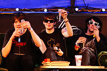Three men who are raising glasses. They are wearing dark clothing