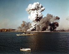 A warship observes as a port explodes in the background