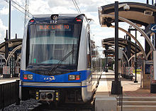 A blue and gray train stopped at a side platformed station with station black and gray station canopies visible.