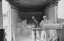 three people loading dusty flour in bags into a boxcar, interior view