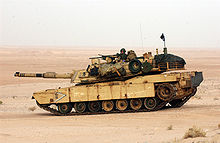 color photo of an Abrams tank sitting in an open sandy field