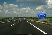 A view of the motorway carriageway from a car, showing two traffic lanes and traffic signs indicating approach to an exit.