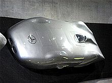 A streamlined silver car with a small transparent canopy on the top for the driver to see through. The Mercedes-Benz logo is displayed prominently on the front.