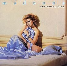 A blond female sits on a bed partially wrapping a mauve colored silk cloth around her. Her short hair is arranged roughly on her head. Above her image, the words "Madonna" is written in blue lowercase. Beneath the word, "Material Girl" is written on the right hand side.