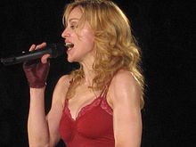 A female blond performer wearing a red top. She is holding a microphone in her brown-gloved right hand.