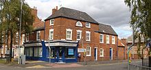 The corner of a terraced street in a suburban setting. The lower storey is a corner shop, advertising as a chiropractic clinic. The building is two storeys high, with some parts three storeys high.