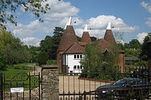 A photograph of two oast houses. There are four cone-shaped kilns topped by white cowls rising from the v-shaped roofs of the houses