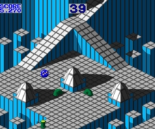 Horizontal rectangular video game screenshot of the arcade version that is a digital representation of a gridded plane with ramps and spikes. A blue marble is near the center of the screen, with moving green tubes below it.