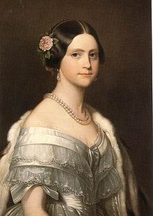 Half-length painted portrait of a brown-haired young woman wearing a white satin ball gown trimmed with lace and bows, and also wearing an ermine stole thrown over one shoulder, a double strand of large pearls around her neck, pearl drop earrings, and a pink camellia arranged in the hair over her right ear.