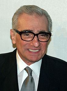 A headshot of a elderly man with grey hair. He is clean shaven and dons rectangular spectacles. He wears a suit and tie.