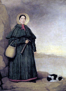 Portrait of a woman in bonnet and long dress holding rock hammer, pointing at fossil next to spaniel dog laying on ground
