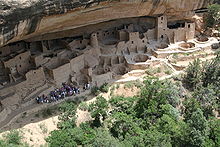 a group of people observing Indian ruins located in a cave.