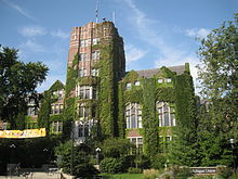 Red brick building with large windows, tall central tower, and green ivy growing on the facade