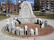  circular monument  in a park made of multiple grey stones.  The large central stone contains a bilingual inscription in memory of women killed by men's violence. Many much smaller irregularly shaped stone shafts are carved with women's names