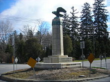 A tall monument sits in the center of an intersection. At the base are the names of nearby locations as well as arrows denoting where the locations are in respect to this intersection.