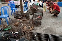 On a street, Western tourists examine several small wire cages containing snakes, lizards, slow lorises, and other exotic animals.