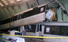 A badly damaged subway car sticks up at an angle where it had partially ridden over another car in an underground station.
