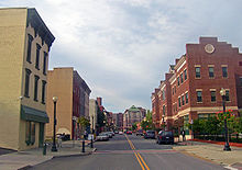 A two-lane city street is flanked on both sides by several multi-story buildings. Taller buildings are visible in the background.