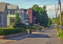A narrow two-lane street is surrounded by houses on its left side.