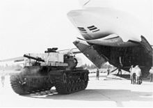 A cargo plane with its access door open, men, and a tank