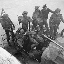 nine British soldiers and one sailor on a small boat at sea. A Union Jack flies from a mast at the rear
