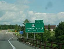 Green exit sign (in French and English) that has the New York State Route 9N symbol with the destinations listed as AuSable Forks and Keeseville.