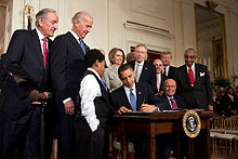 Obama signs bill at desk while others look on.