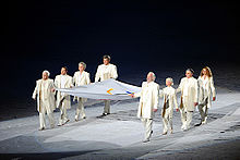 Eight people carrying a large flag within a spotlight