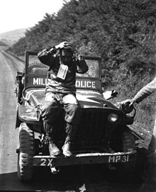 A man sits on a jeep with his hands on his head