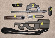 Photo of a disassembled PS90 carbine, showing the major component groups: 1. hammer group, 2. barrel and optical sight group, 3. butt plate, 4. magazine, 5. moving parts group, 6. frame and trigger group.
