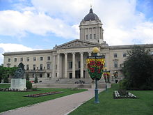 A large concrete building with Classical-style columns and a green dome topped by a golden statue