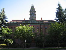 A two-story brick building with a tall tower is partially obscured by trees.
