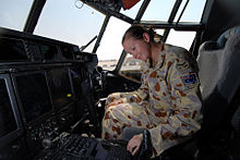 A woman wearing a camouflaged military uniform sitting in the cockpit of an aircraft