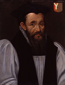 A head-and-shoulders portrait of Richard Bancroft. The portrait portrays Bancroft on a grey background, wearing a white shirt with a black vest. Bancroft is wearing a black cap and has collar length brown hair. Over Bancroft's left shoulder is a red and brown family crest