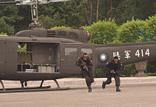 Two men in military uniform getting off an helicopter. They are both running and carrying a weapon.
